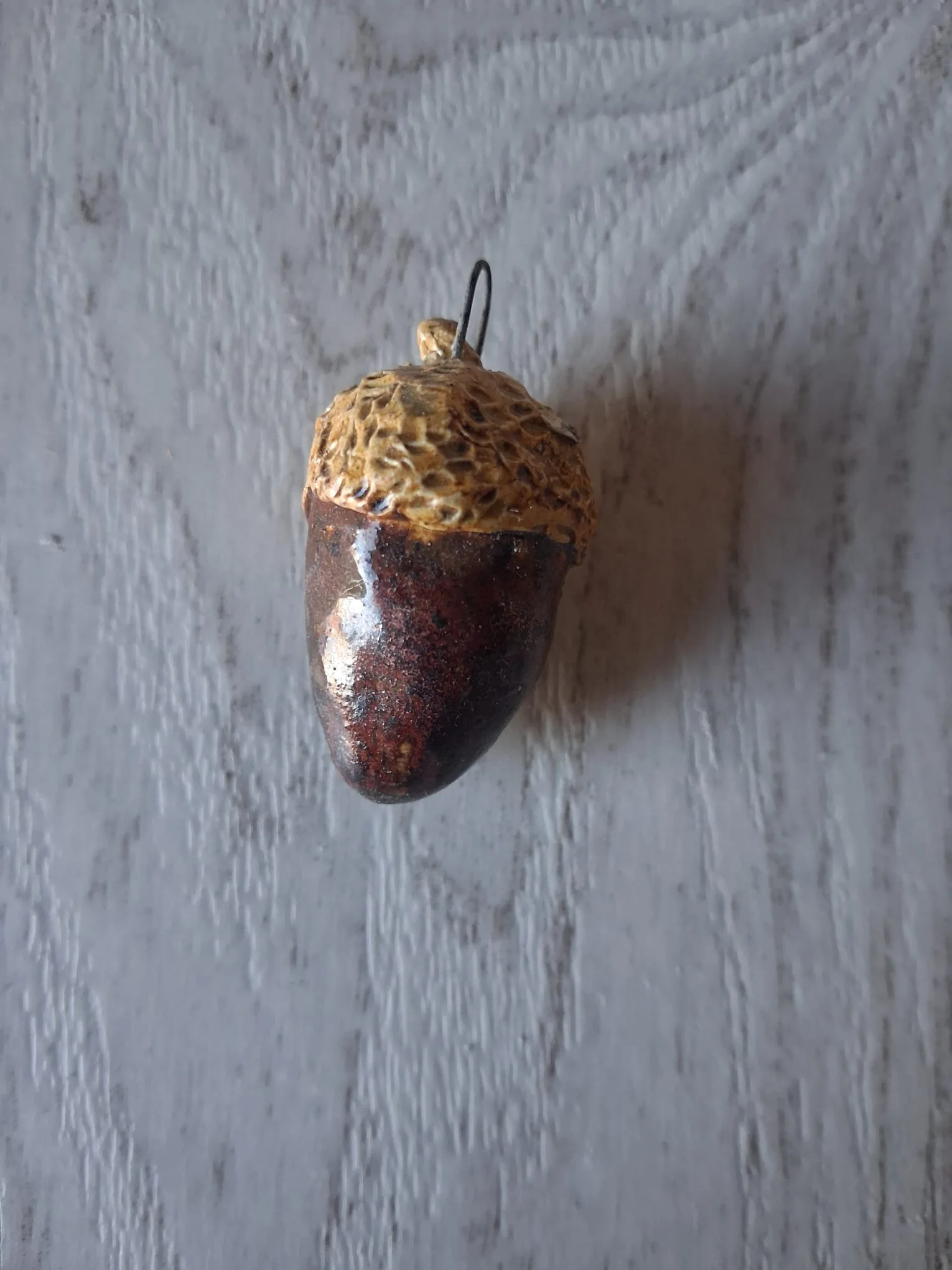 Adorno de Navidad de gres con forma de bellota de unos 4 cm, de cuerpo marrón chocolate brillante y capuchón dorado texturizado, con anilla de alambre para colgar, esmaltado a mano en Valladolid — CreArte