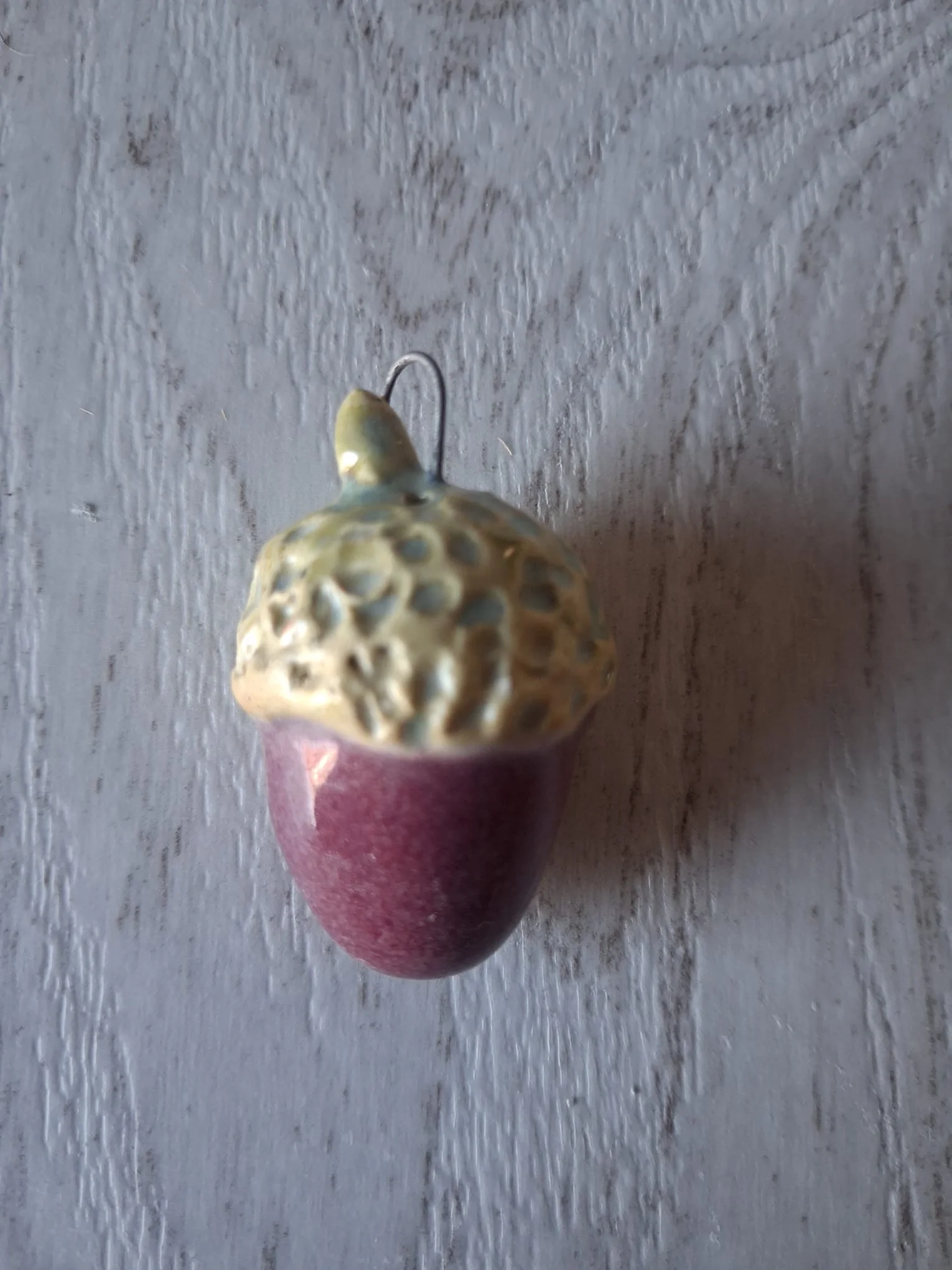 Adorno de Navidad de gres con forma de bellota de unos 4 cm, de cuerpo morado ciruela brillante y capuchón verde amarillento con relieve de círculos, con anilla de alambre para colgar, esmaltado a mano en Valladolid — CreArte