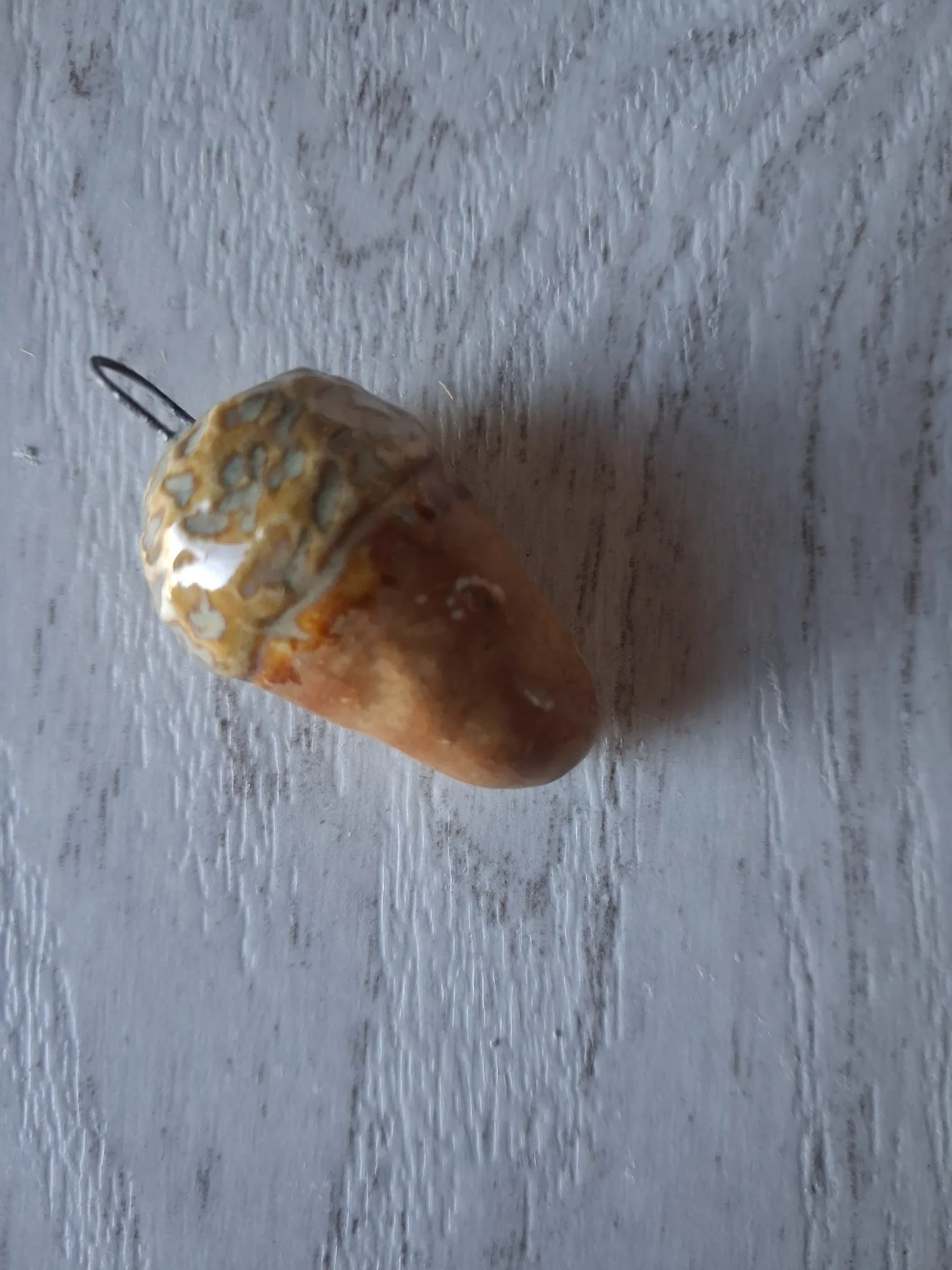 Adorno de Navidad de gres con forma de bellota de unos 4 cm, de cuerpo naranja y marrón degradado y capuchón ocre con manchas gris azuladas, con anilla de alambre para colgar, esmaltado a mano en Valladolid — CreArte