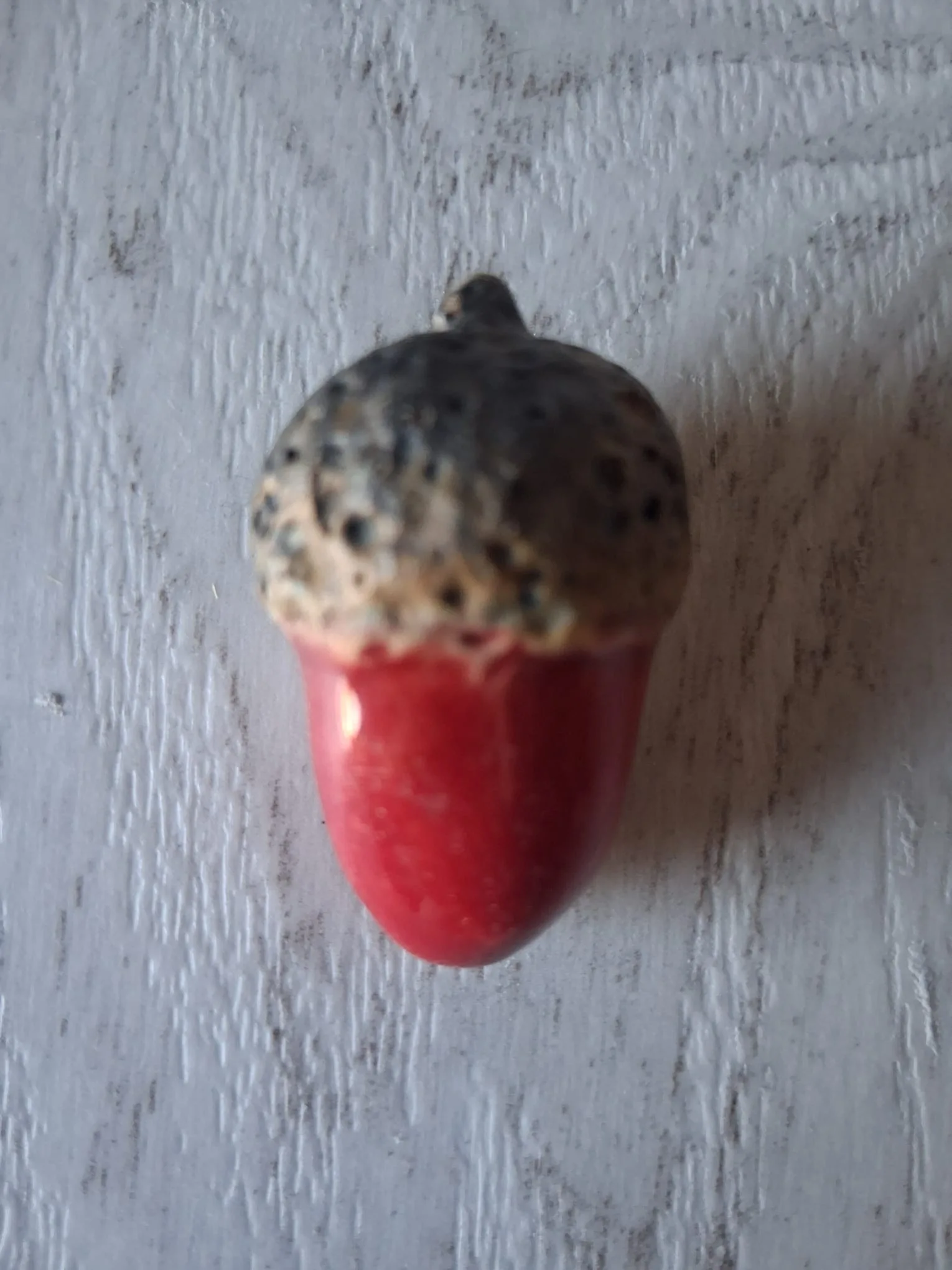 Adorno de Navidad de gres con forma de bellota de unos 4 cm, de cuerpo rojo brillante y capuchón rugoso gris y crema con puntos oscuros, esmaltado a mano en Valladolid — CreArte