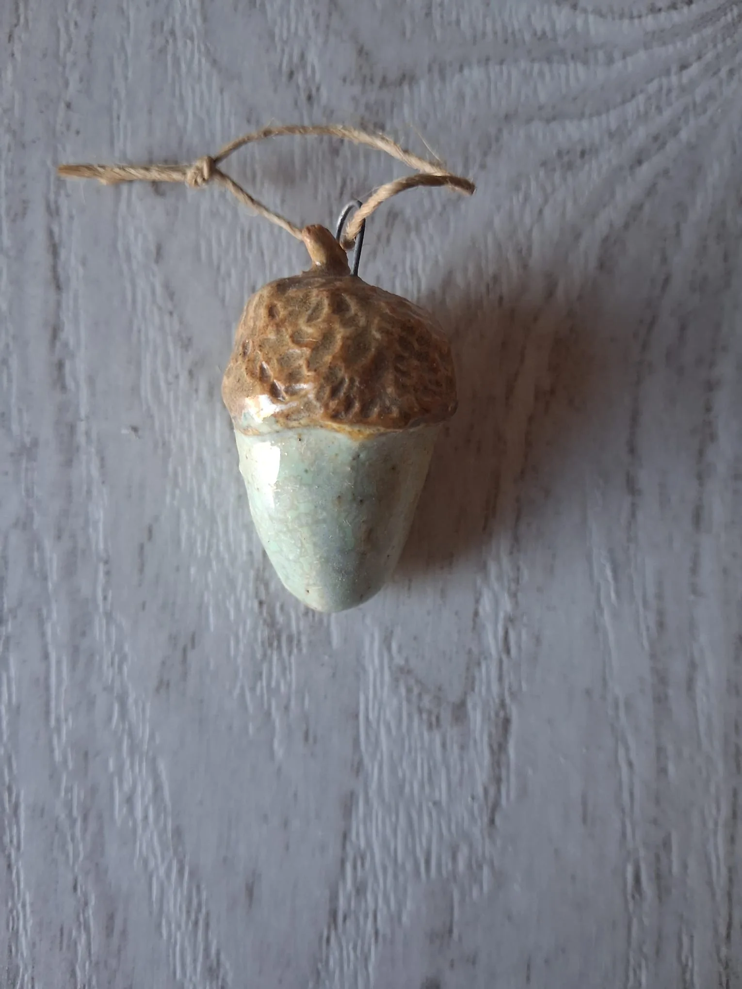 Adorno de Navidad de gres con forma de bellota de unos 4 cm, de cuerpo verde menta craquelado y capuchón marrón en relieve, con anilla de alambre y cordel de yute para colgar, esmaltado a mano en Valladolid — CreArte