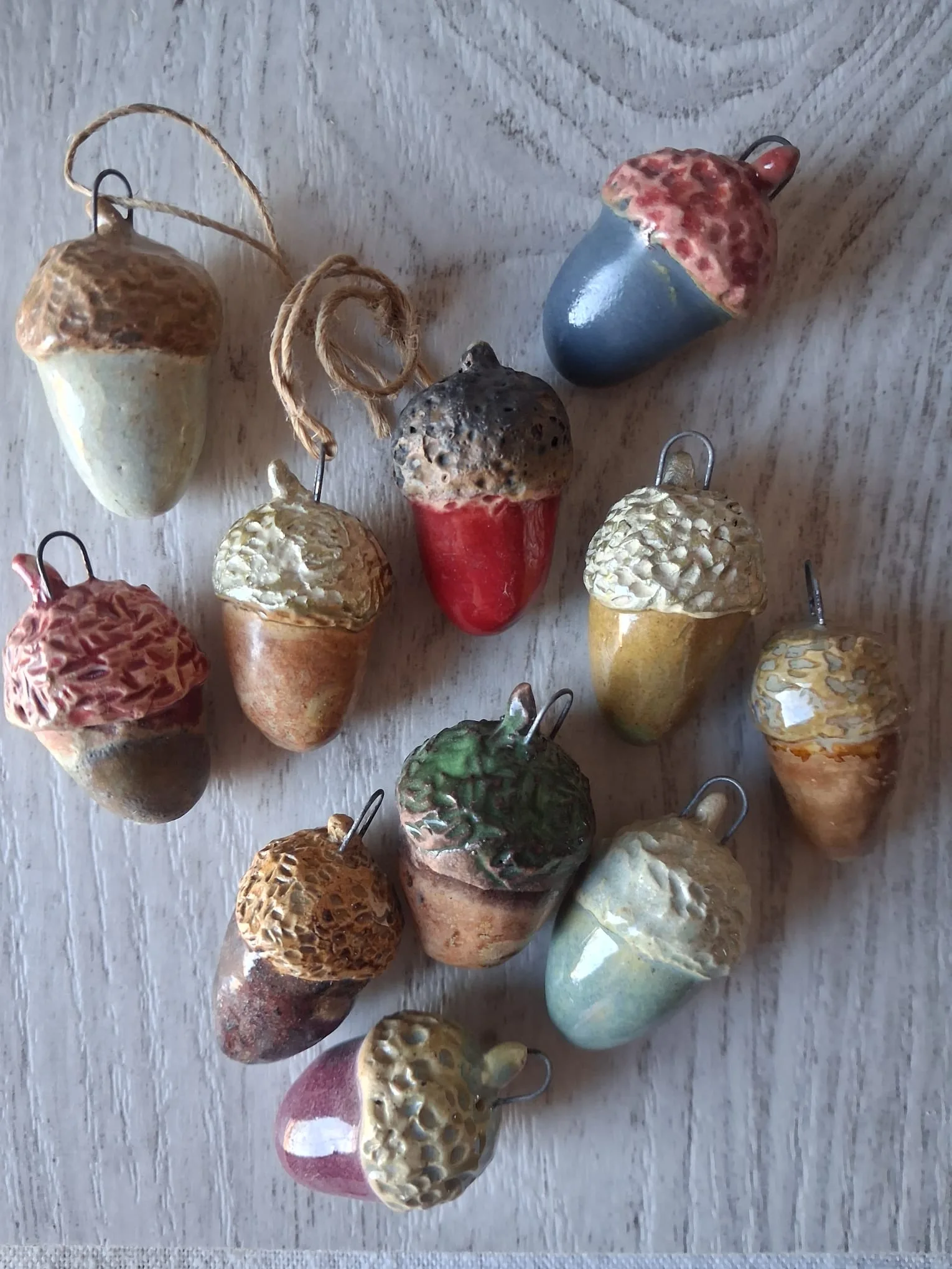 Surtido de bellotas de cerámica de gres de unos 4 cm esmaltadas a mano para el árbol de Navidad, cada una con un color y un capuchón distinto, con anilla de alambre o cordel de yute para colgar, hechas en Valladolid — CreArte