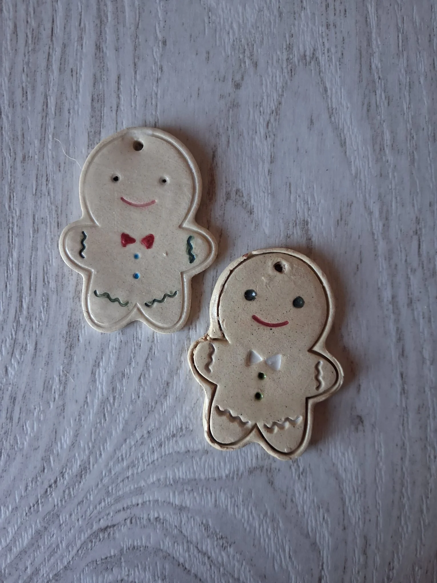 Dos adornos de Navidad de cerámica con forma de galleta de jengibre, uno con pajarita roja y botones azules y otro con pajarita blanca y botones verdes, esmaltados a mano en Valladolid — CreArte
