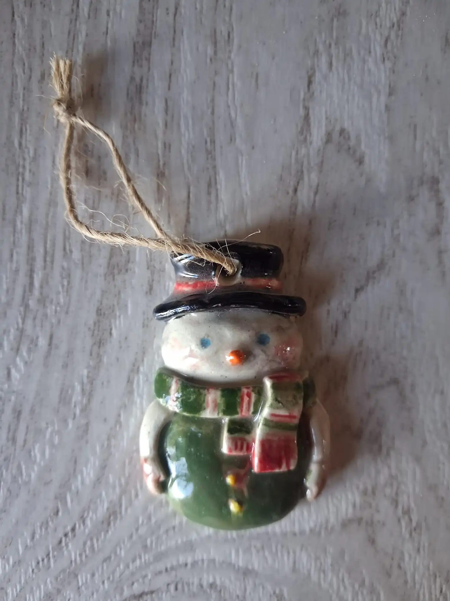Adorno de Navidad de cerámica con muñeco de nieve de sombrero negro, bufanda a rayas verdes y rojas y cuerpo verde, con cordel de yute, hecho a mano en Valladolid — CreArte