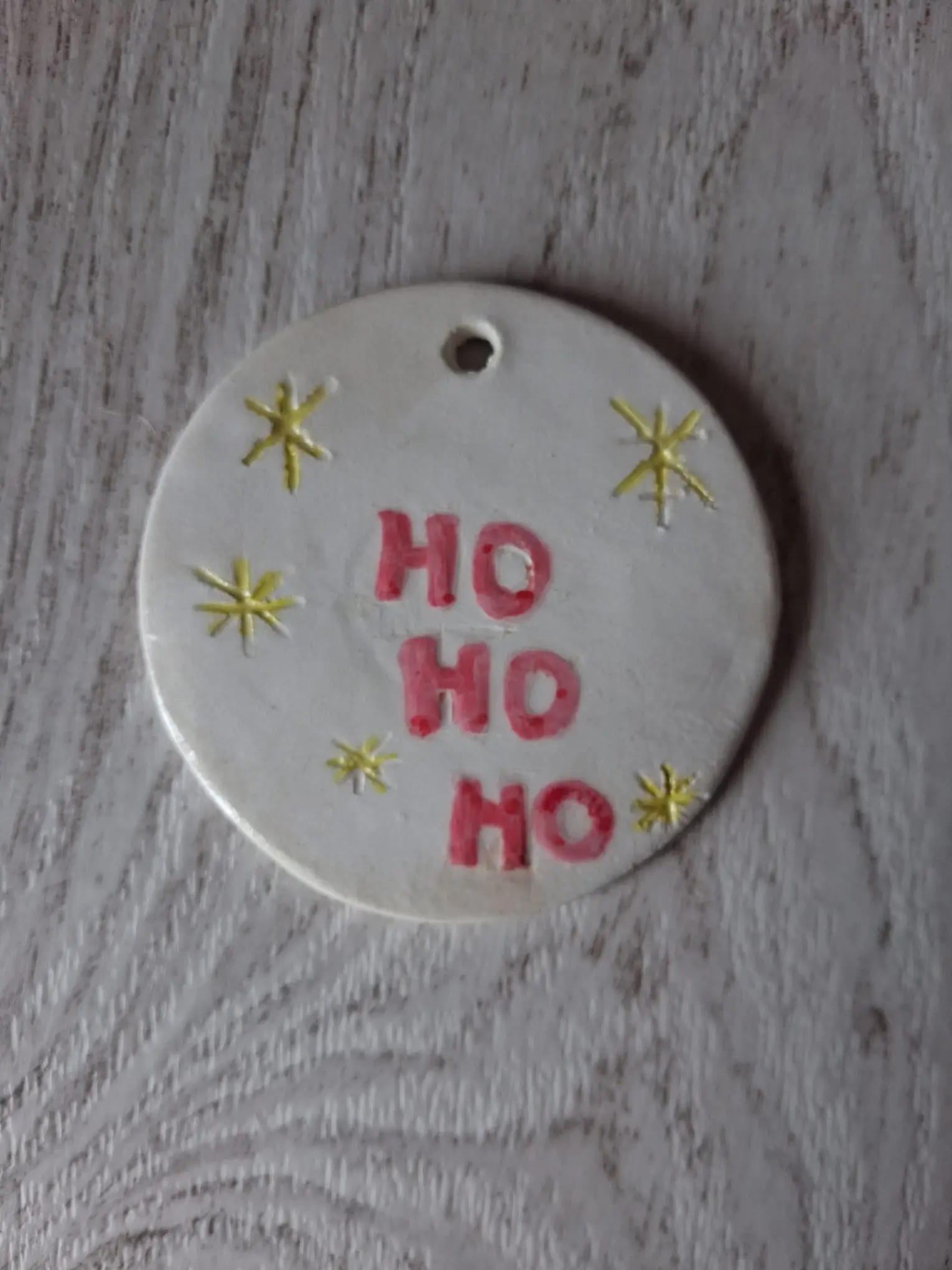 Adorno de Navidad de cerámica redondo blanco con texto HO HO HO en rojo y estrellas amarillas, personalizable, pintado a mano en Valladolid — CreArte