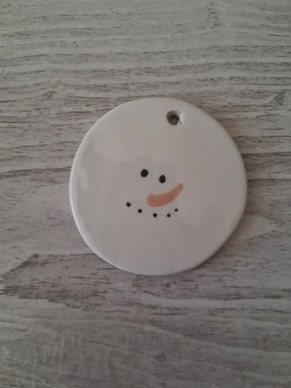 Adorno de Navidad de cerámica redondo blanco con cara de muñeco de nieve, ojos negros, nariz de zanahoria naranja y sonrisa de puntos negros, personalizable, pintado a mano en Valladolid — CreArte