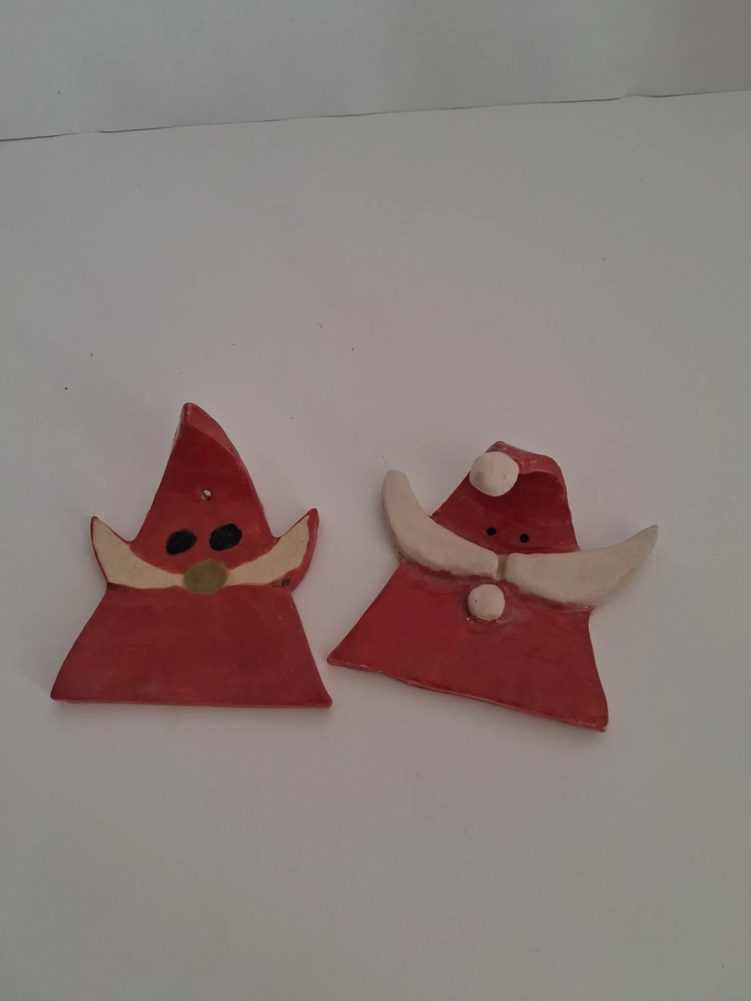 Dos adornos de Navidad de cerámica con figuras triangulares rojas: un gnomo con bigote crema y nariz verde y un Papá Noel con gorro de pompón y bigote blanco, personalizables, hechos a mano en Valladolid — CreArte