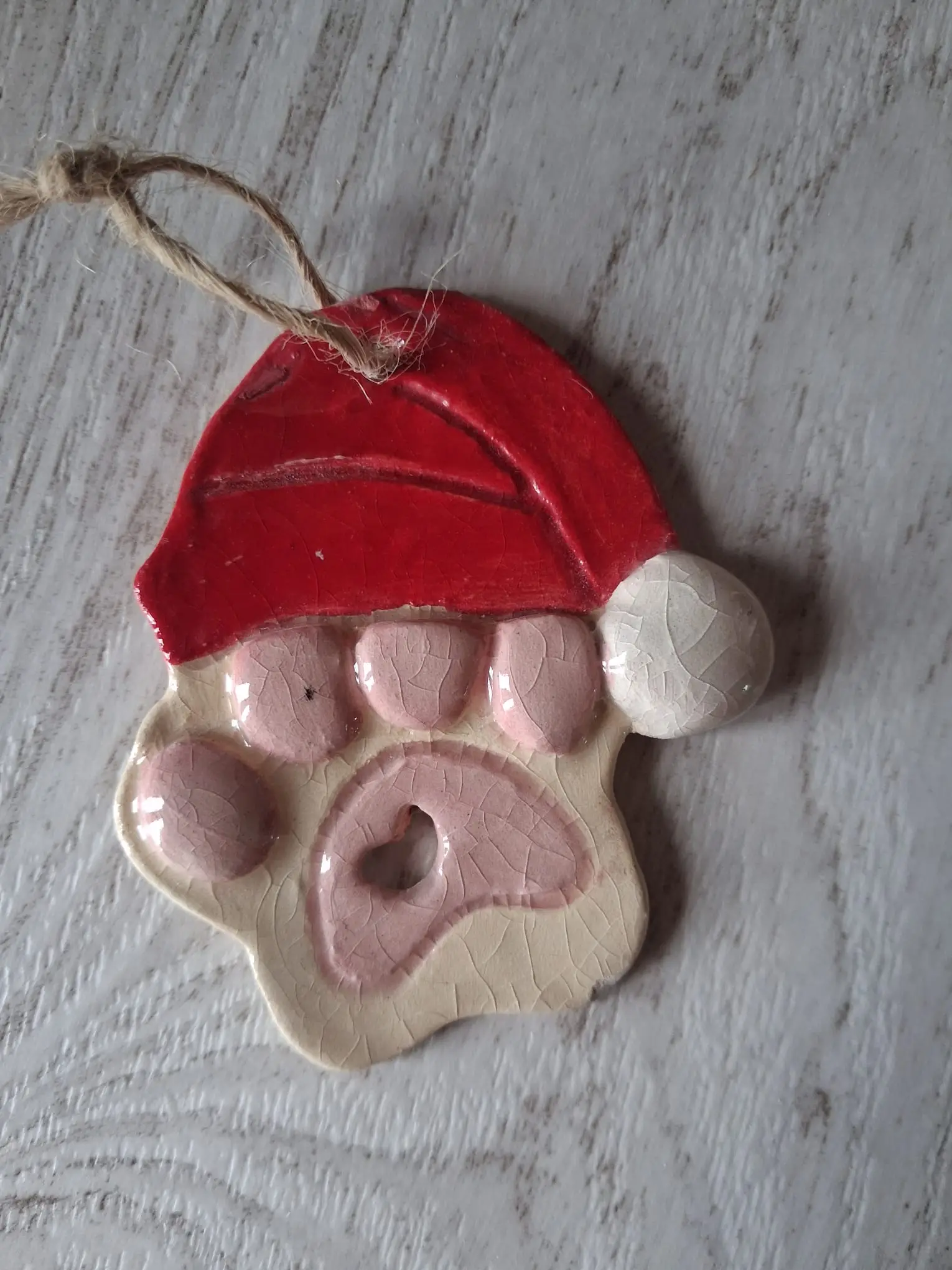 Adorno de Navidad de cerámica con una pata de almohadillas rosas y gorro de Papá Noel rojo con pompón blanco, con cordel de yute, hecho a mano en Valladolid — CreArte