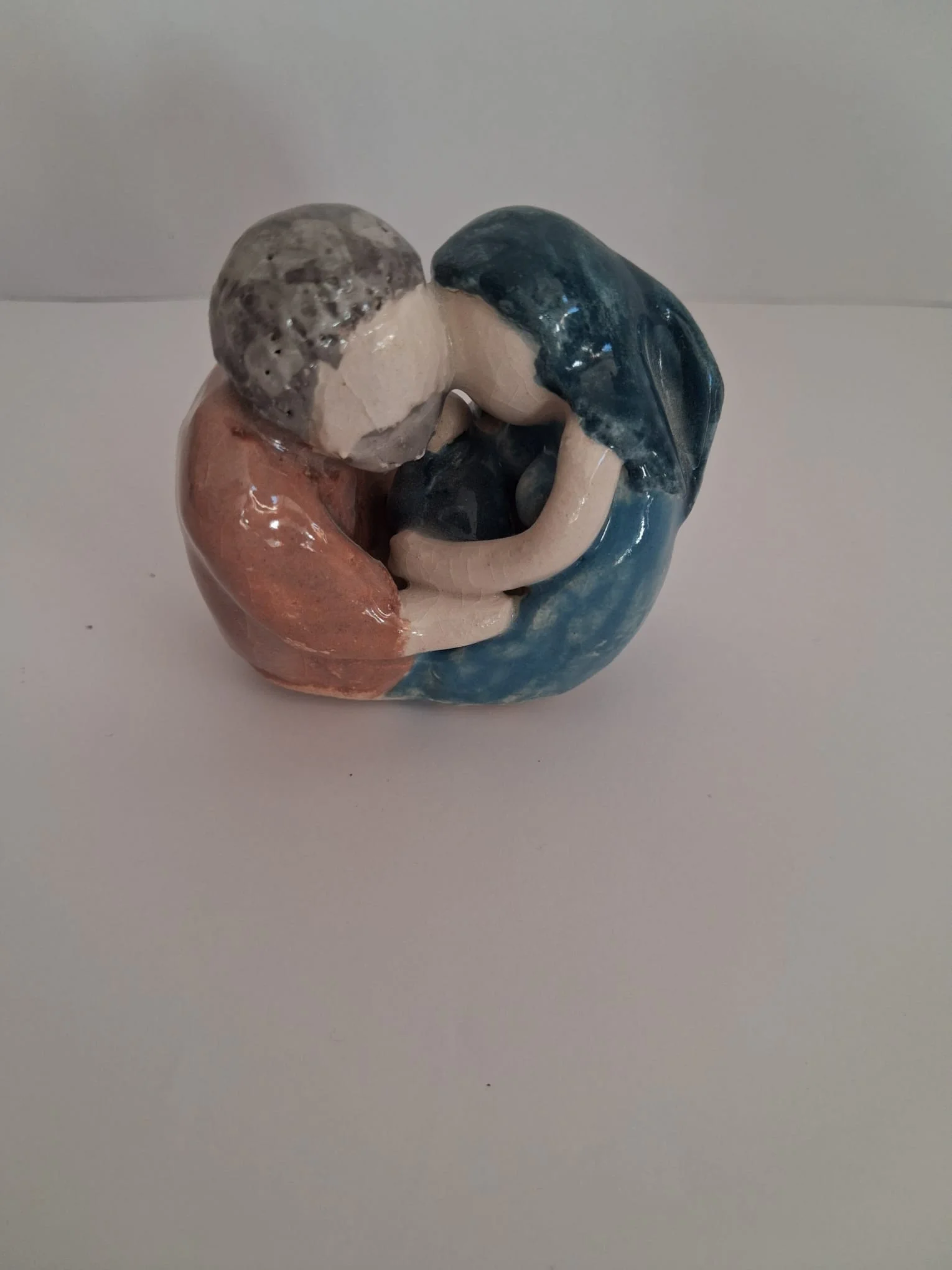 Belén de Navidad de cerámica esmaltada con la Sagrada Familia abrazada: San José con túnica marrón y pelo gris y la Virgen con manto azul, con el Niño en brazos entre ambos, hecho a mano en Valladolid — CreArte