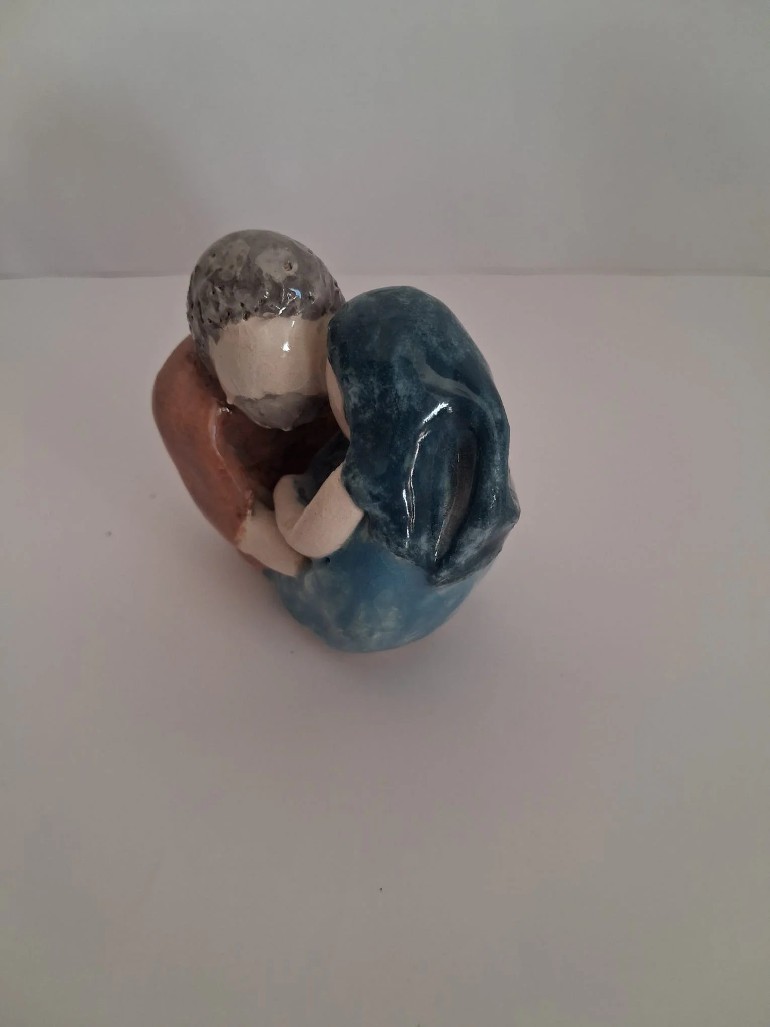 Belén de Navidad de cerámica esmaltada con la Sagrada Familia abrazada, vista lateral: San José con túnica marrón y pelo gris y la Virgen con manto azul, hecho a mano en Valladolid — CreArte