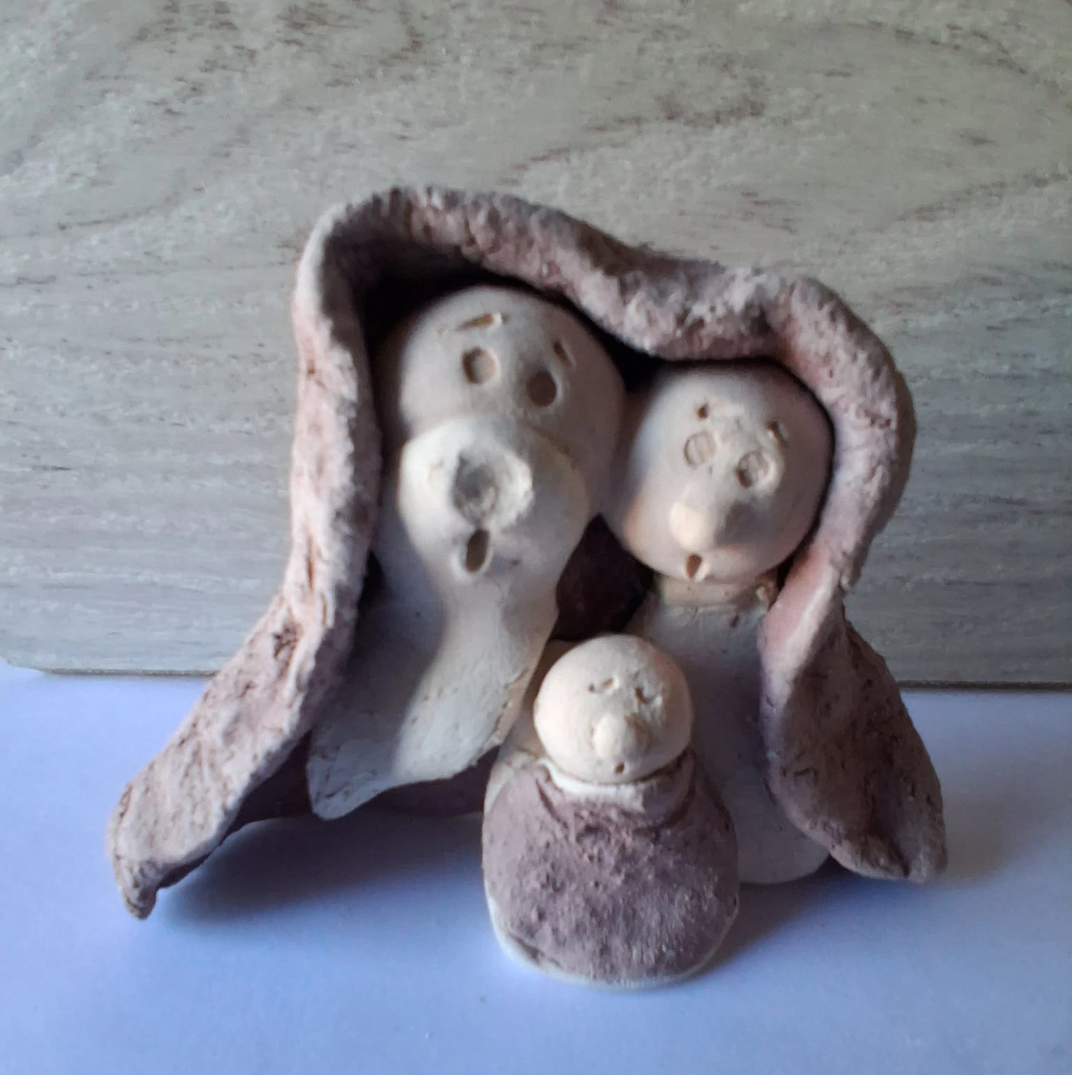 Belén de Navidad de cerámica artesanal con la Sagrada Familia, tres figuras de loza blanca bajo un manto rugoso de tono rosado, hecho a mano en Valladolid — CreArte