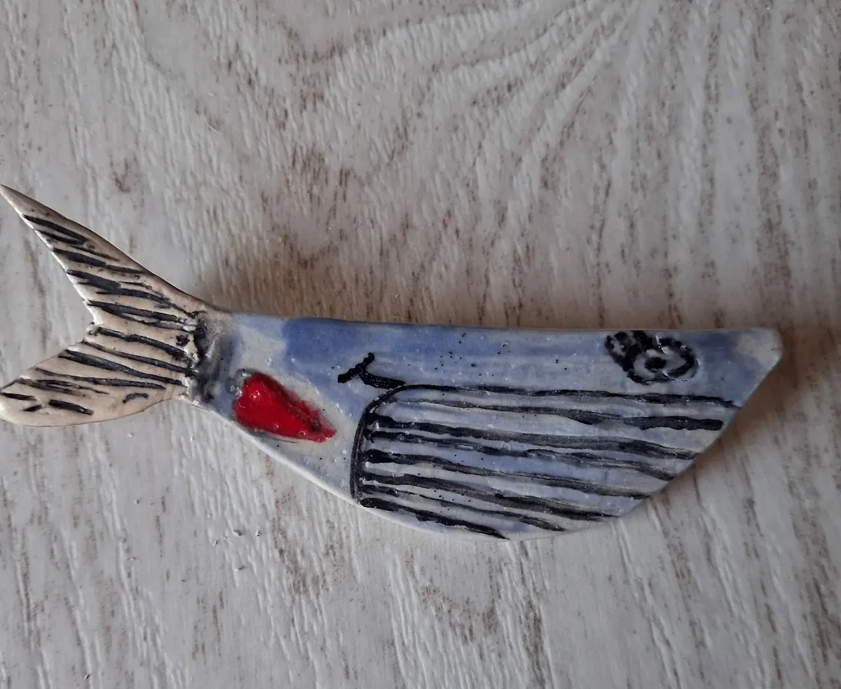 Broche de cerámica con forma de ballena en azul con detalles rayados y un corazón rojo