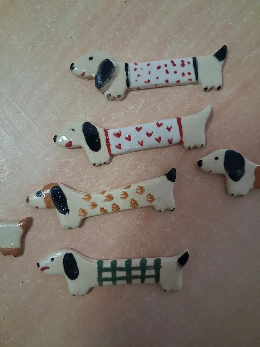 Colección de broches de cerámica con forma de perro salchicha crudos pintados a mano con lunares rojos, corazones rojos, huellas naranjas y una verja verde
