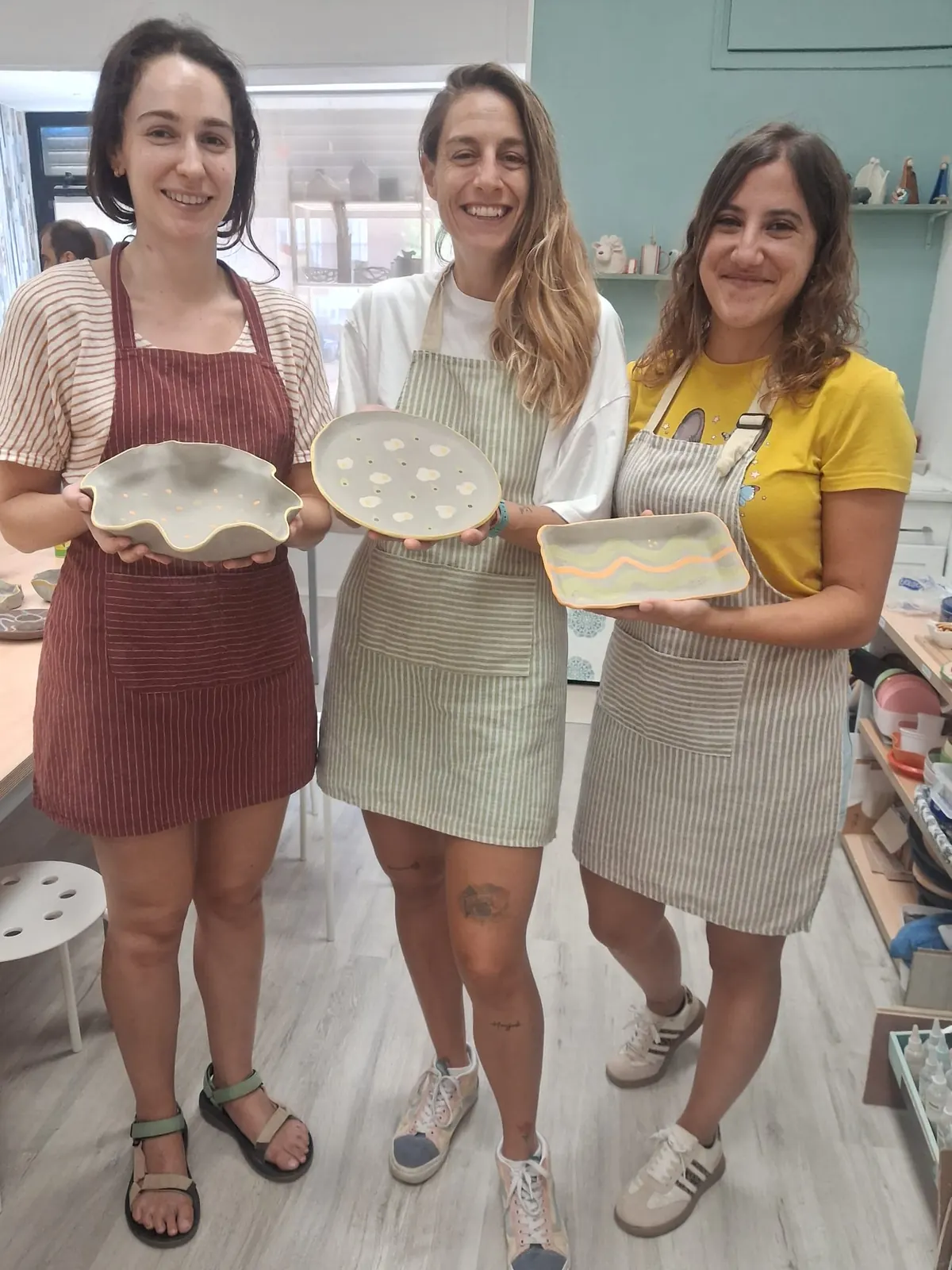 Tres amigas sonriendo y mostrando orgullosas los platos de cerámica que han pintado juntas en un taller de grupo en Valladolid