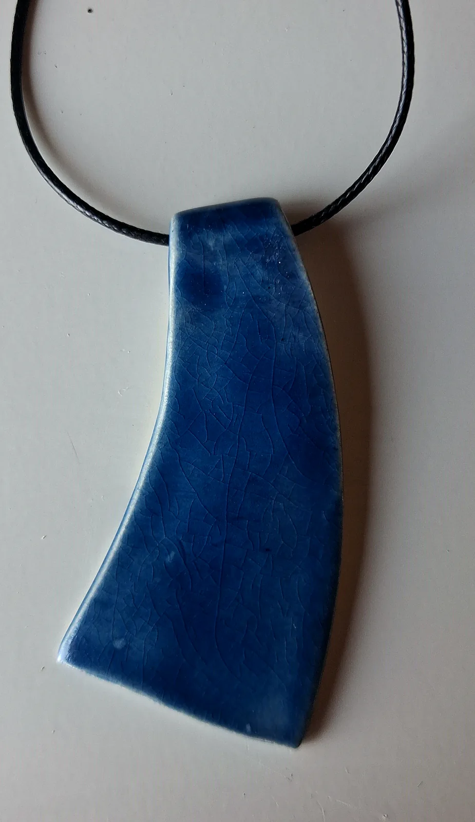 Collar de cerámica artesanal con colgante curvo en azul marino craquelado, montado sobre cordón negro, hecho a mano en el taller CreArte Valladolid