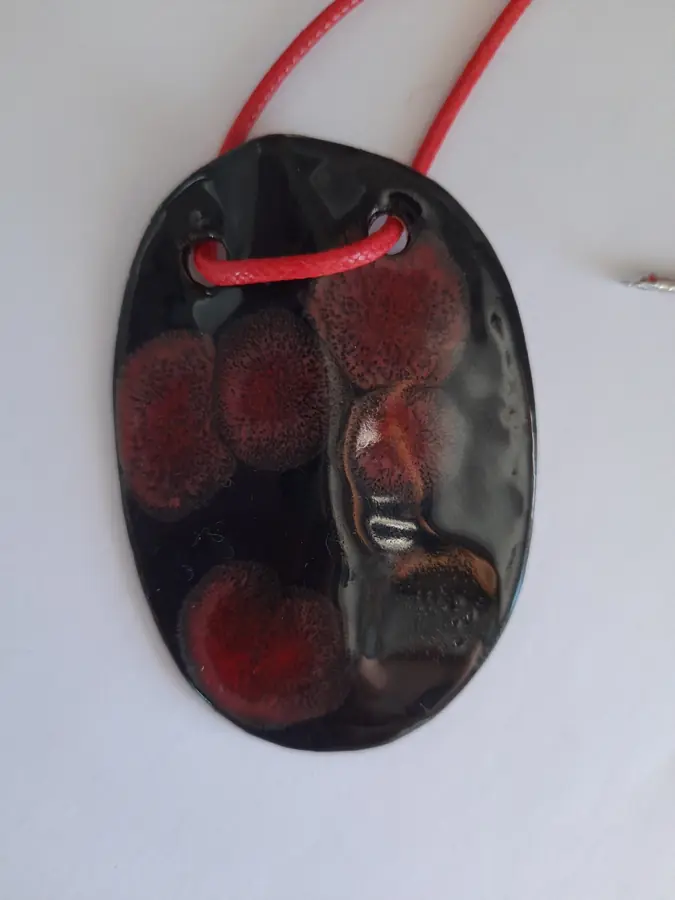 Colgante de cerámica ovalado negro con manchas rojas sobre cordón rojo, Colección Geométrica, taller CreArte Valladolid