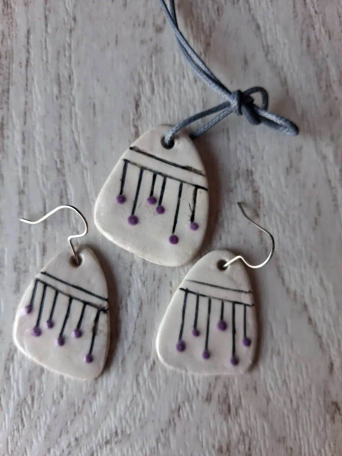 Conjunto artesanal de cerámica blanca con líneas negras y bolitas moradas: collar y pendientes a juego, hecho a mano en taller CreArte Valladolid