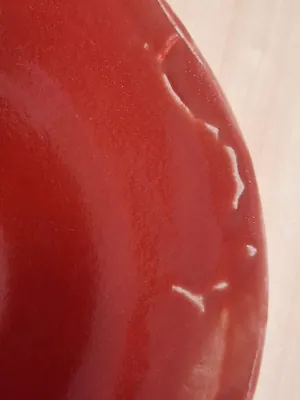 Esmalte rojo escamado y saltado en el borde de un cuenco de cerámica, mostrando el bizcocho blanco expuesto, taller CreArte Valladolid