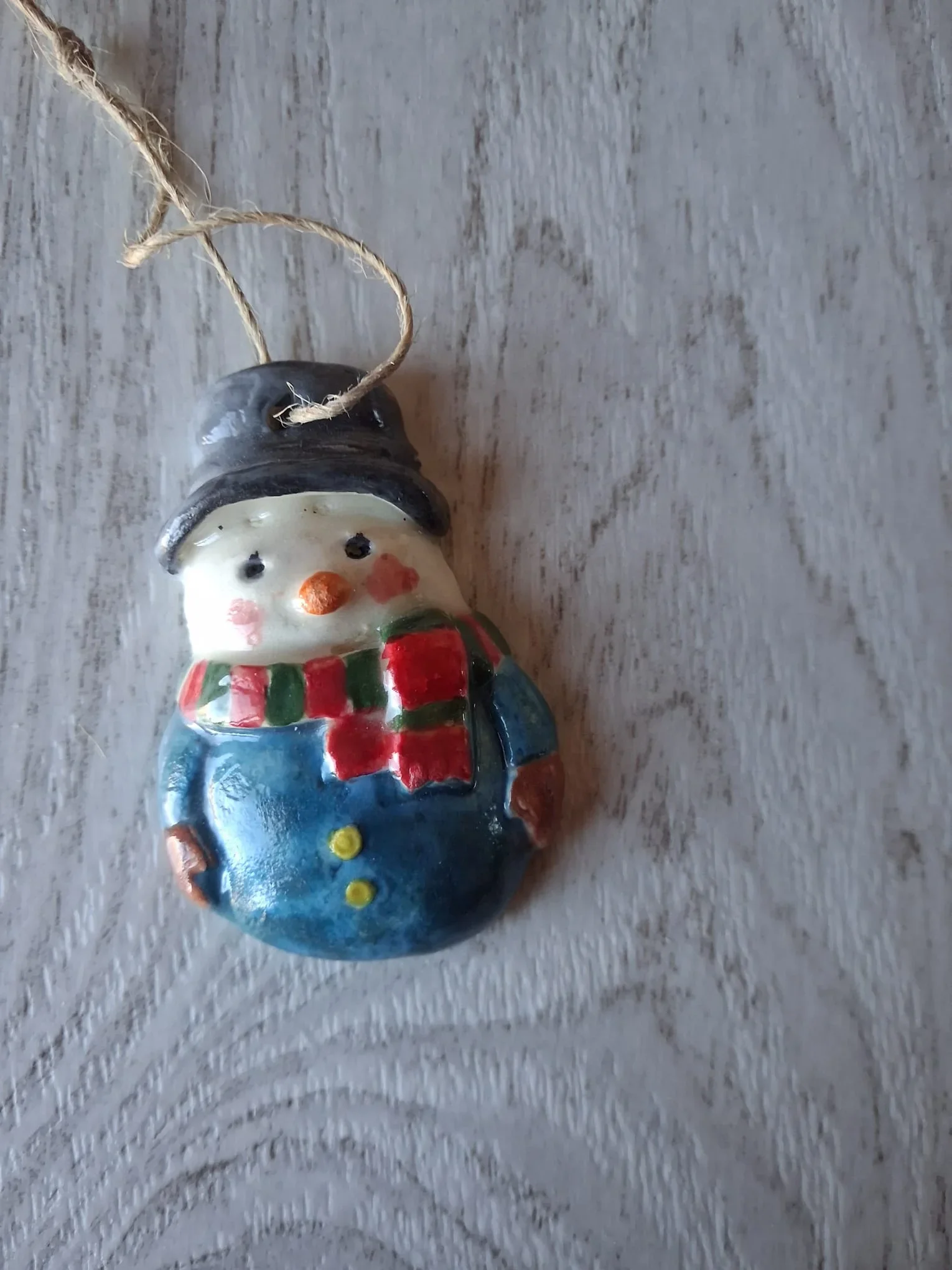 Figura de Navidad de cerámica con muñeco de nieve de sombrero negro, bufanda a rayas rojas y verdes, cuerpo azul con botones amarillos y manoplas marrones, con cordel de yute, hecha a mano en Valladolid — CreArte