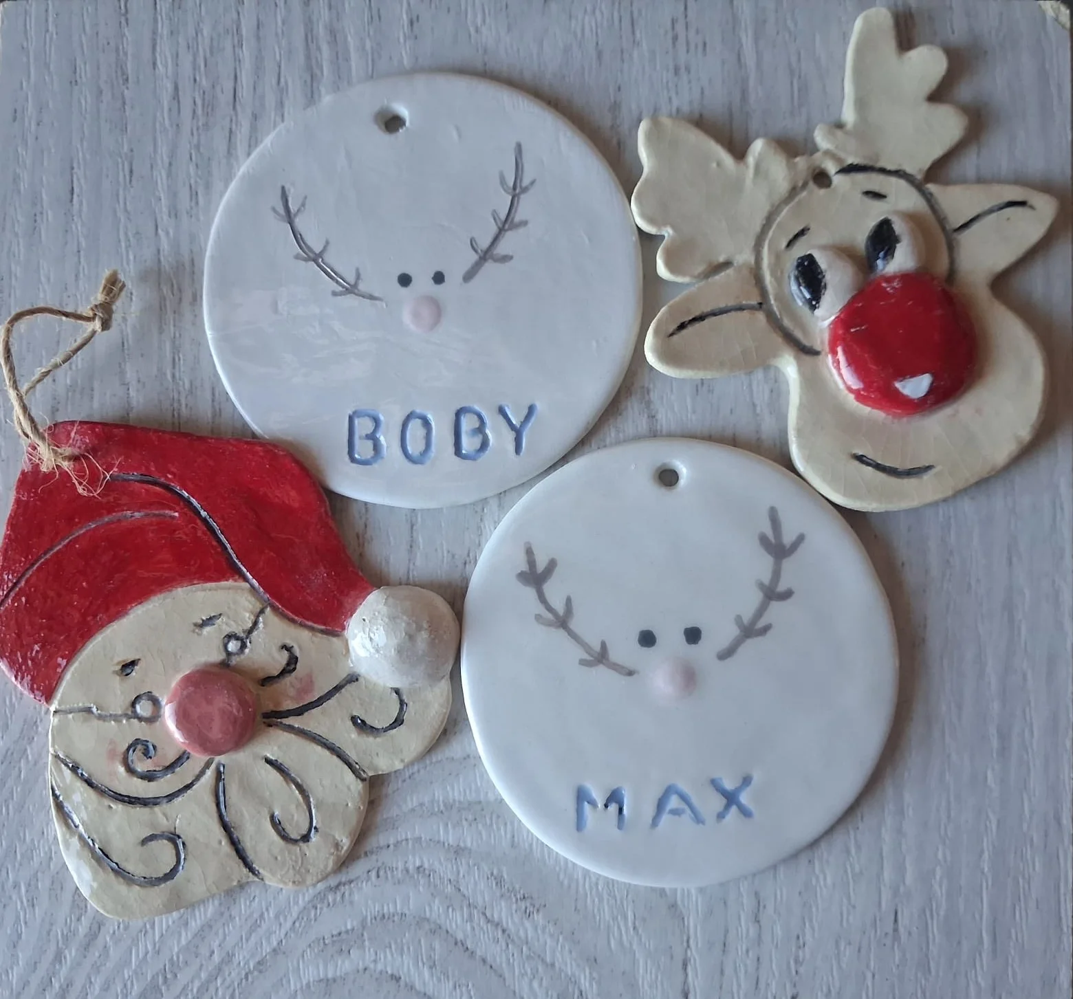 Figuras de Navidad de cerámica: cabeza de Papá Noel con gorro rojo y barba rizada, reno de nariz roja y dos adornos redondos blancos con cara de reno y los nombres Boby y Max, hechos a mano en Valladolid — CreArte