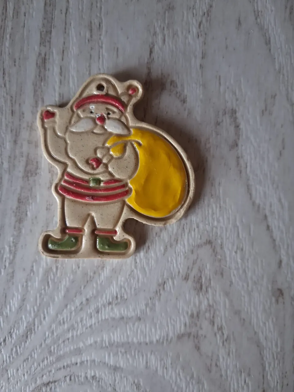 Figura de Navidad de cerámica con Papá Noel saludando, gorro rojo con pompón, barba blanca, jersey a rayas rojas, botas verdes y un saco amarillo brillante a la espalda, con agujero para colgar, de unos 5-6 cm, hecha a mano en Valladolid — CreArte