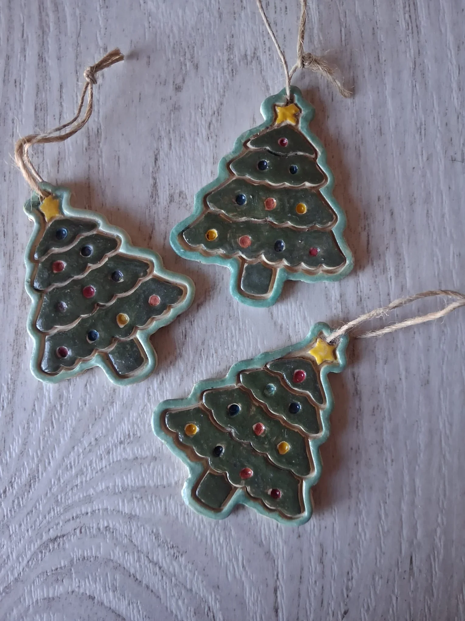 Tres figuras de Navidad de cerámica con forma de abeto verde esmaltado con borde turquesa, estrella amarilla en la copa, bolitas de colores y cordel de yute para colgar, hechas a mano en Valladolid — CreArte