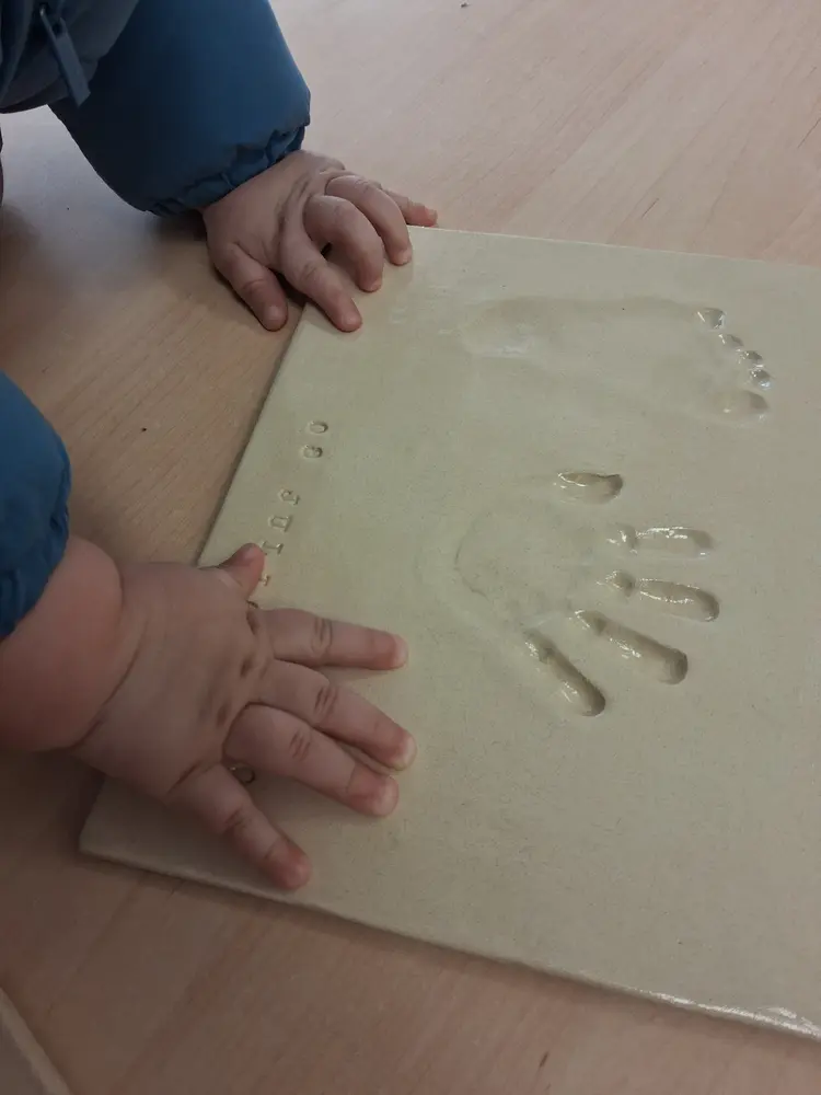 Manos de un bebé apoyadas sobre la pieza de cerámica mientras se toman sus huellas de nacimiento en el taller CreArte de Valladolid