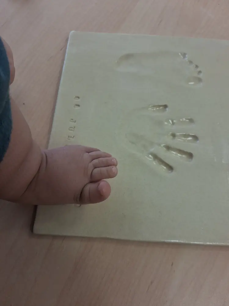 Pie de un bebé recién nacido junto a la pieza de cerámica con su huella de mano y pie recién marcadas, recuerdo de nacimiento personalizado en CreArte Valladolid