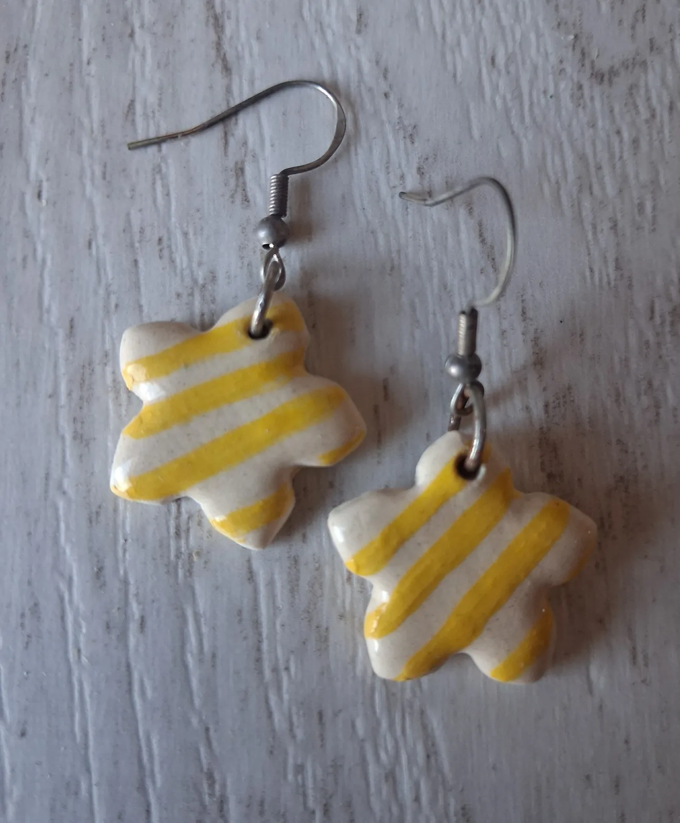 Pendientes de cerámica con forma de flor y rayas amarillas sobre fondo crema