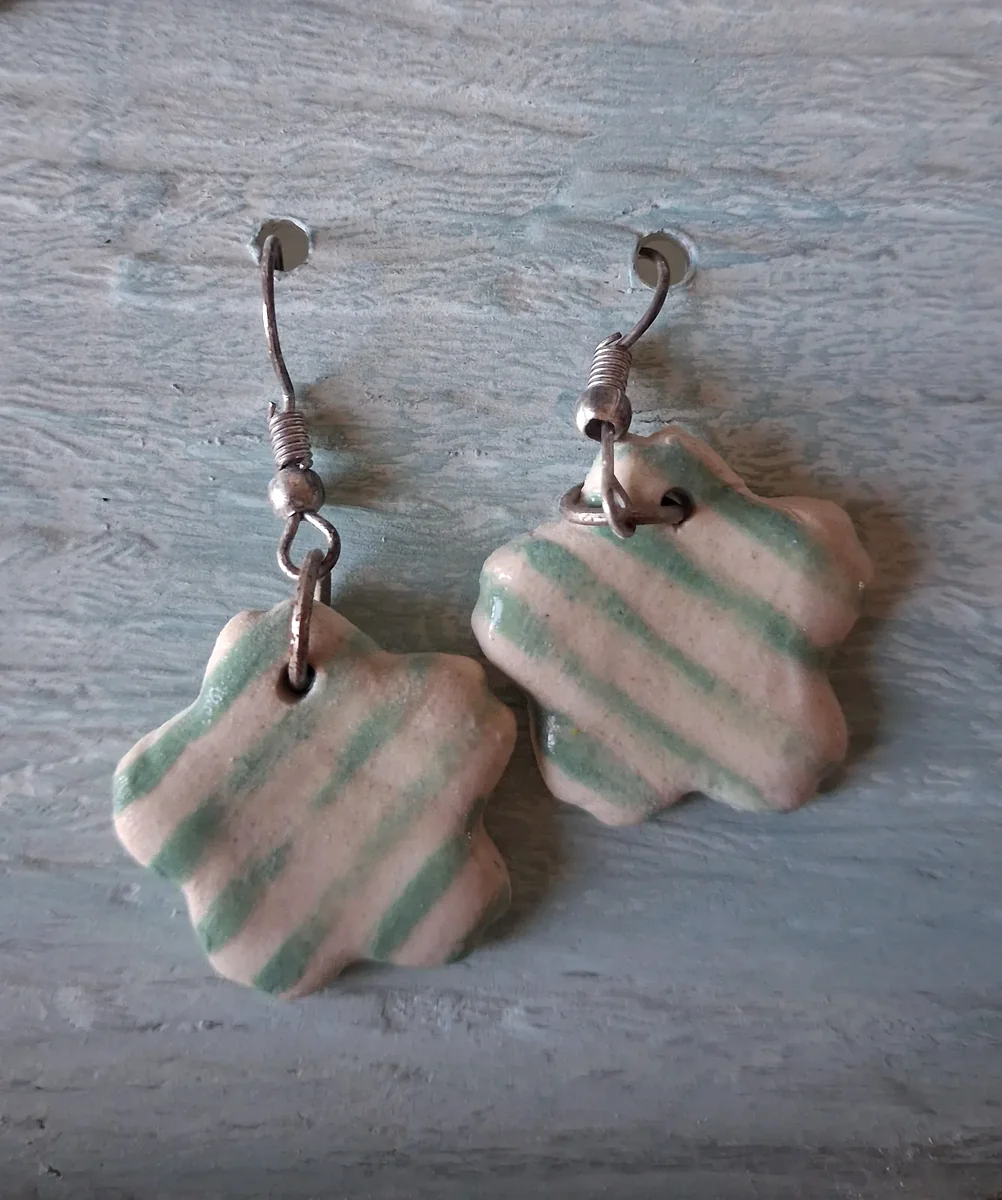 Pendientes de cerámica con forma de flor y rayas verdes sobre fondo crema